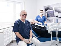 Ersin Kamberci im Behandlungszimmer – ZFA und Patient im Hintergrund